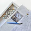 A paint-by-numbers kit for 'The Witcher' is laid out on a white surface. It includes a canvas, numbered paint pots, brushes, and a reference image. Produktbild-Vorschau