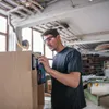 A man is using a cordless oscillating tool to sand a wooden cabinet in a workshop. Anteprima dell’immagine prodotto