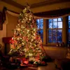 A decorated Christmas tree with presents underneath, in a room with a window showing a twilight scene. Voir les images du produit