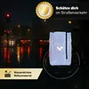 A reflective bicycle bag is attached to a bicycle wheel in a rainy urban environment at night, with traffic lights and car headlights visible in the background. Produktbild-Vorschau