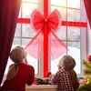 Two children looking out a window decorated with a large red bow for Christmas. Náhled obrázku produktu