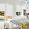 A bedroom with large windows covered by white roller blinds. A bed and a bench are in the foreground. Produktbild-Vorschau