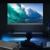 A person is watching a movie on a large screen projector in a dark room, with a mini projector in the foreground. Náhľad obrázku produktu