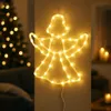 A lit-up angel silhouette decoration hangs on a wall, with a blurred Christmas tree in the background. Produktbild-Vorschau