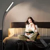 A woman is reading a book on a bed, illuminated by a floor lamp. Produktbild-Vorschau