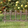 A decorative metal fence in a garden setting with yellow flowers in the background. Produktbild-Vorschau