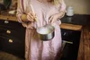 A person in a pink dress is whisking a white mixture in a small pot in a kitchen. Podgląd zdjęcia produktu