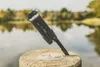 A black multi-tool is stuck into a wooden post with a body of water and trees in the background. Produktbild-Vorschau