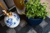 A close-up shot of a decorative ceramic ball with blue floral patterns and a small golden dog figurine on top, next to a potted green plant in a dark blue ribbed planter. Podgląd zdjęcia produktu