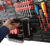 A hand is holding a black cable winder attached to a tool wall. Produktbild-Vorschau