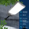 A solar-powered street lamp mounted on a textured wall, with green leaves in the foreground and background. Text and icons describing the product's features are on the right side. Produktbild-Vorschau