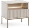 A cream-colored nightstand with a fluted drawer and gold metal legs, illuminated by an integrated LED light. Produktbild-Vorschau