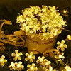 A string of yellow flower-shaped lights is draped over a miniature bicycle and a basket, with more lights scattered on the ground. Produktbild-Vorschau