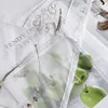 A close-up of a white fabric with embroidered details and printed images of green apples and text. Produktbild-Vorschau