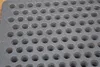 A close-up view of a gray metal grate with a pattern of circular holes. Voir les images du produit