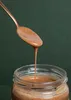 A spoon is lifting almond butter from a jar. Produktbild-Vorschau