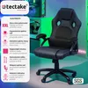 A black ergonomic office chair is shown in front of a background with computer equipment and ambient lighting. Náhled obrázku produktu