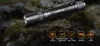 A black Fenix E20 flashlight is placed on a rocky, mossy surface. Náhled obrázku produktu