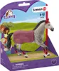 A toy horse figurine in its retail packaging, with a scenic background depicting rolling hills and trees. Several cartoon-like girls are also visible on the left side of the packaging. Produktbild-Vorschau