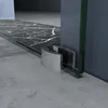 A close-up view of a glass sliding door's bottom track and a metallic guide, set against a marble floor and a concrete floor. Produktbild-Vorschau