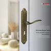 A close-up of an antique bronze door handle set mounted on a door, with a blurred interior scene in the background. Produktbild-Vorschau