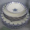 A stack of white ceramic plates and bowls with blue decorative trim and a blue floral design in the center of the top bowl. Produktbild-Vorschau