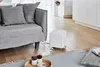 A white humidifier sits on a wooden floor next to a gray sofa, with a rug and a book in the foreground. Produktbild-Vorschau