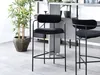 Two black bar stools in a modern setting with a plant and shelving unit. Produktbild-Vorschau