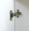 A close-up view of a cabinet hinge attached to a white surface. Náhled obrázku produktu