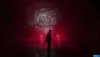 A person stands in a dark, red-lit environment with a swirling vortex-like image projected on a wall in the background. Podgląd zdjęcia produktu