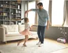 A father and daughter are dancing in a living room. Voir les images du produit