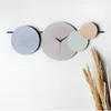 A modern wall clock with overlapping circular elements in muted colors, mounted on a white wall. Produktbild-Vorschau