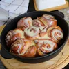 A close-up view of cinnamon rolls in a black cast iron pan, drizzled with a white glaze. Produktbild-Vorschau
