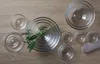 A collection of clear glass bowls and a sprig of green leaves arranged on a wooden surface. Anteprima dell’immagine prodotto