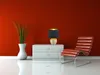 A modern living room scene with a red wall, a white chest of drawers, a table lamp, a plant in a vase, and a lounge chair. Náhled obrázku produktu