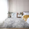 A bedroom scene with a large gray shaggy rug in the foreground, a nightstand with a lamp and a picture frame, and a bed with a yellow throw blanket. Náhled obrázku produktu