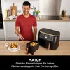 A man is in a kitchen, holding tongs with food, next to a dual-zone air fryer. Produktbild-Vorschau