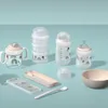 A collection of baby feeding items, including bottles, a sippy cup, a stackable container, a bowl, and cutlery, arranged on a light blue background. Produktbild-Vorschau