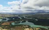 An aerial view of a winding river flowing through a lush green landscape with mountains in the distance under a cloudy sky. Anteprima dell’immagine prodotto