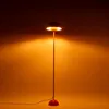 A red floor lamp with a dome-shaped shade is illuminated against a warm orange background. Podgląd zdjęcia produktu