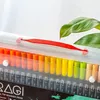 A close-up view of a clear plastic case containing rows of colorful marker pens, with a green leaf in the background. Produktbild-Vorschau