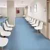 A waiting room in a medical facility with rows of white chairs and a blue floor. Podgląd zdjęcia produktu