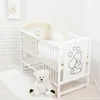 A white crib with teddy bear themed bedding and a teddy bear toy next to it. Voir les images du produit