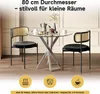 A round glass-top dining table with two chairs, set in a room with a light-colored wall and wooden floor. Decorative elements like a coffee maker and fruit are on the table. Náhľad obrázku produktu