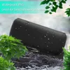 A black portable speaker is placed on wet rocks near water, with green leaves in the foreground and background. The image suggests the speaker is waterproof and suitable for outdoor use. Produktbild-Vorschau