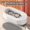 A white ultrasonic cleaner with glasses inside, placed on a desk with a watch and a gray mat. Produktbild-Vorschau