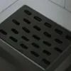 A close-up view of a metal grate with rectangular slots, likely a drain cover. Produktbild-Vorschau