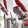 A person is emptying the dustbin of a vacuum cleaner into a trash can, and a close-up of the vacuum cleaner's dustbin. Produktbild-Vorschau