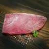 A raw flank steak is presented on a wooden surface, seasoned with salt and peppercorns, and garnished with a sprig of parsley. Produktbild-Vorschau