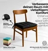 A black chair cushion on a wooden chair, with text overlays and a stack of colorful cushions in the corner. Produktbild-Vorschau